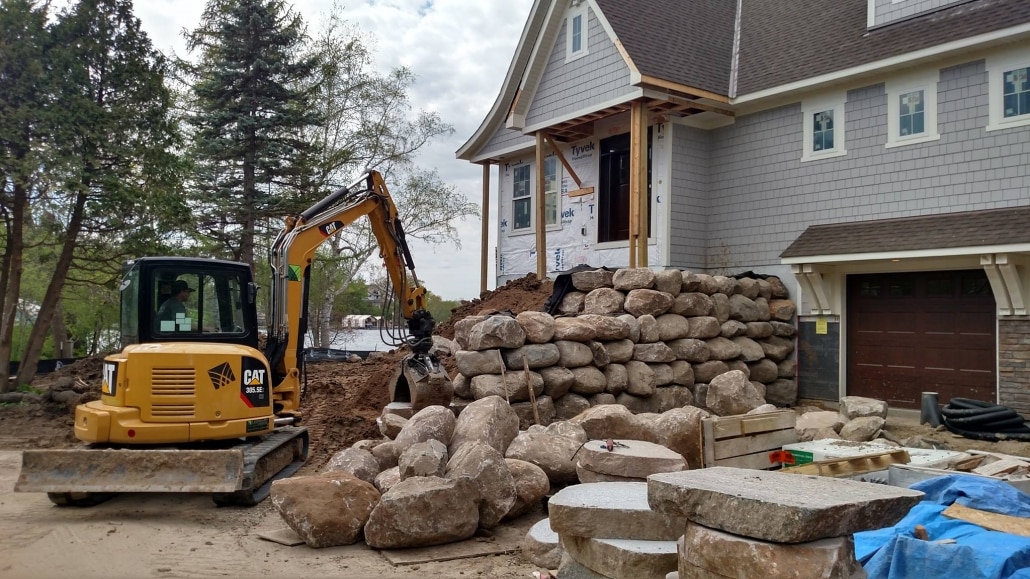 An excavator operator at Landscapes Unlimited hand selects and carefully places boulders for this retaining wall to allow for a walkout garage.  