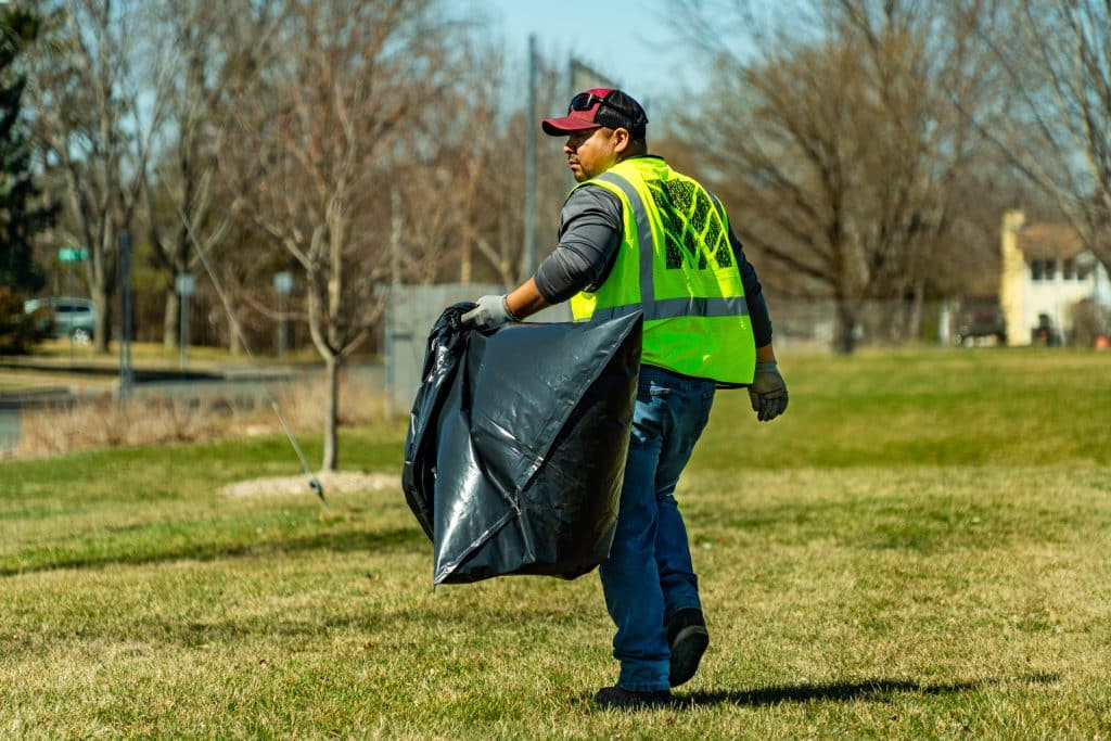 Landscapes Unlimited Maintenance crew cleaning up a local park with garbage bag in hand.