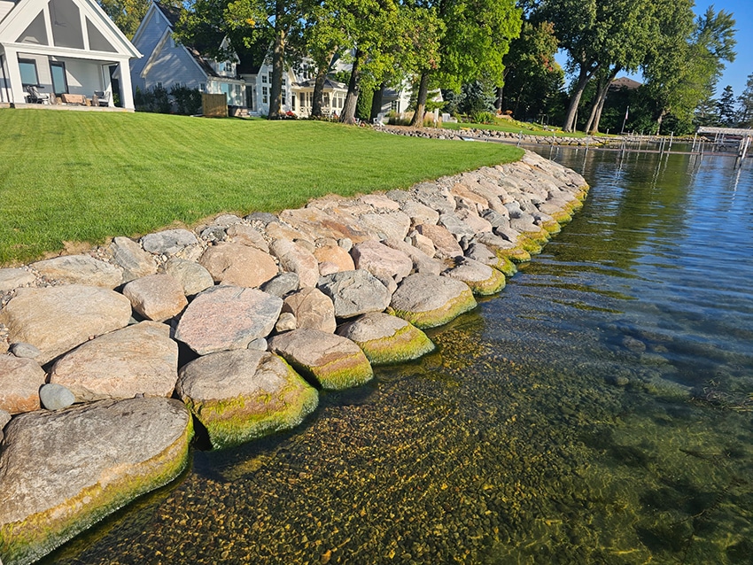Boulder rip rap shoreline protecting a manicured lakefront lawn with luxury homes in Deephaven, MN