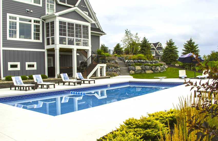 Inground pool with white concrete patio pavers and lounge chairs behind a gray two-story home in Eden Prairie, MN