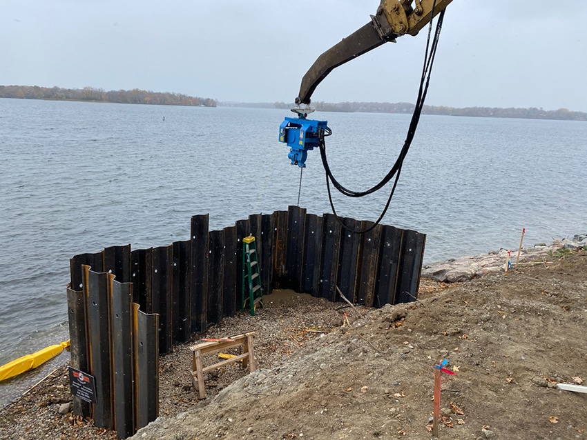 Excavator driving steel sheet piling for a new seawall installation on a lakeshore in Excelsior, MN